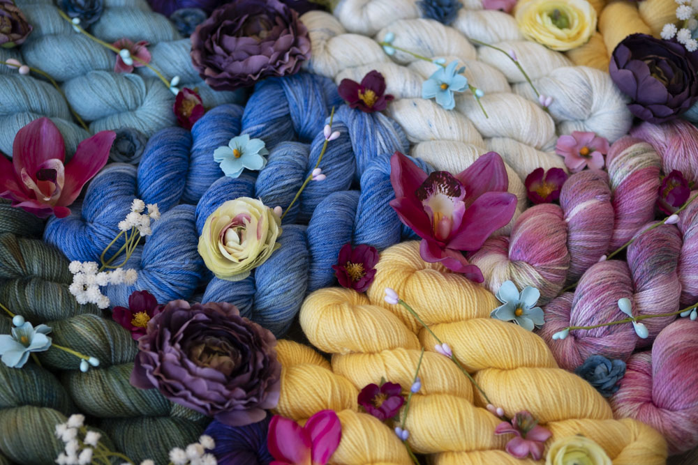 Colorful hand-dyed yarn and dried flowers in shades of yellow, blue, magenta, cream, pine green, and sky blue