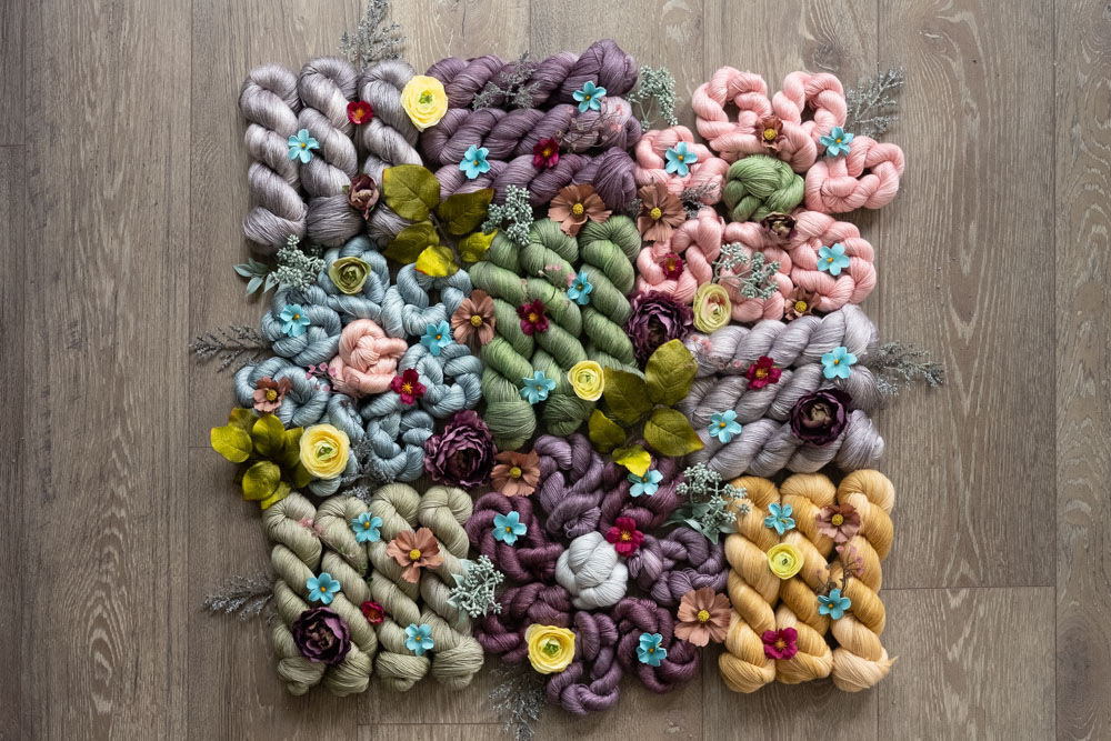 A pile of hand-dyed yarn in shades of sage green, sky blue, mauve, grey and more