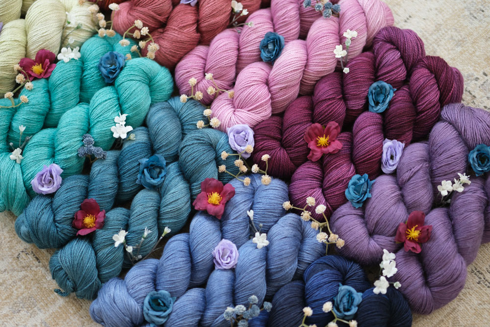 A close-up of colorful, hand-dyed yarn skeins in shades of purple, fuchsia, pink, turquoise, teal, blue and more