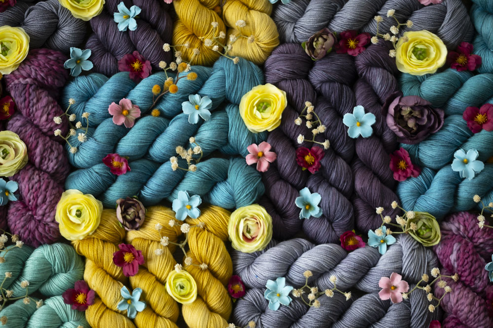A pile of colorful, hand-dyed yarns in shades of dandelion yellow, turquoise, grey, fuchsia, and more